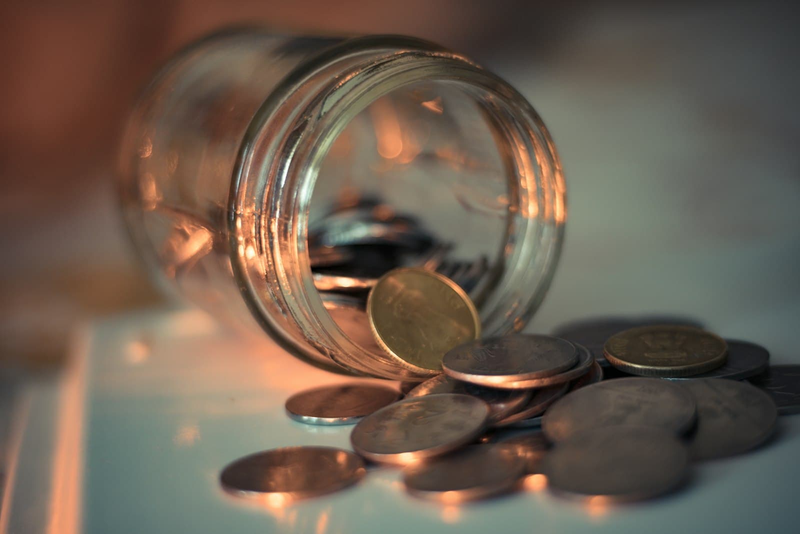 A glass jar tipped on its side with coins spilling onto a table