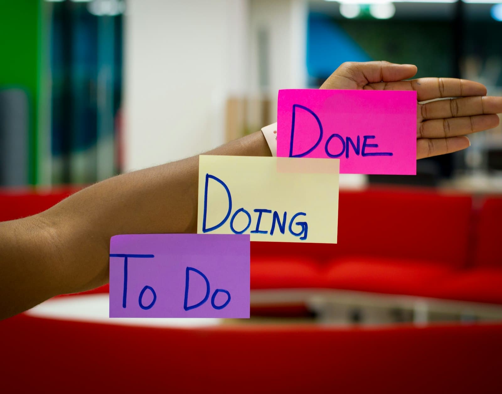 Sticky notes reading To Do, Doing and Done balanced on an outstretched arm