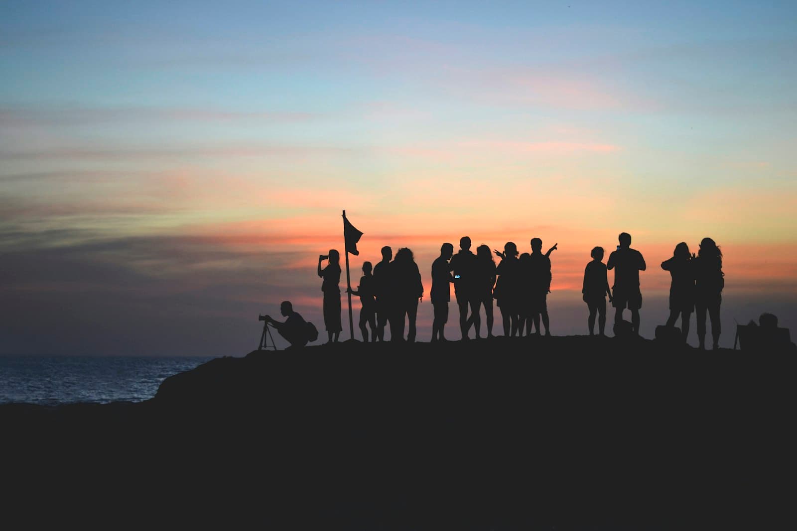 A crowd of friends silhouetted against a sunset by the sea